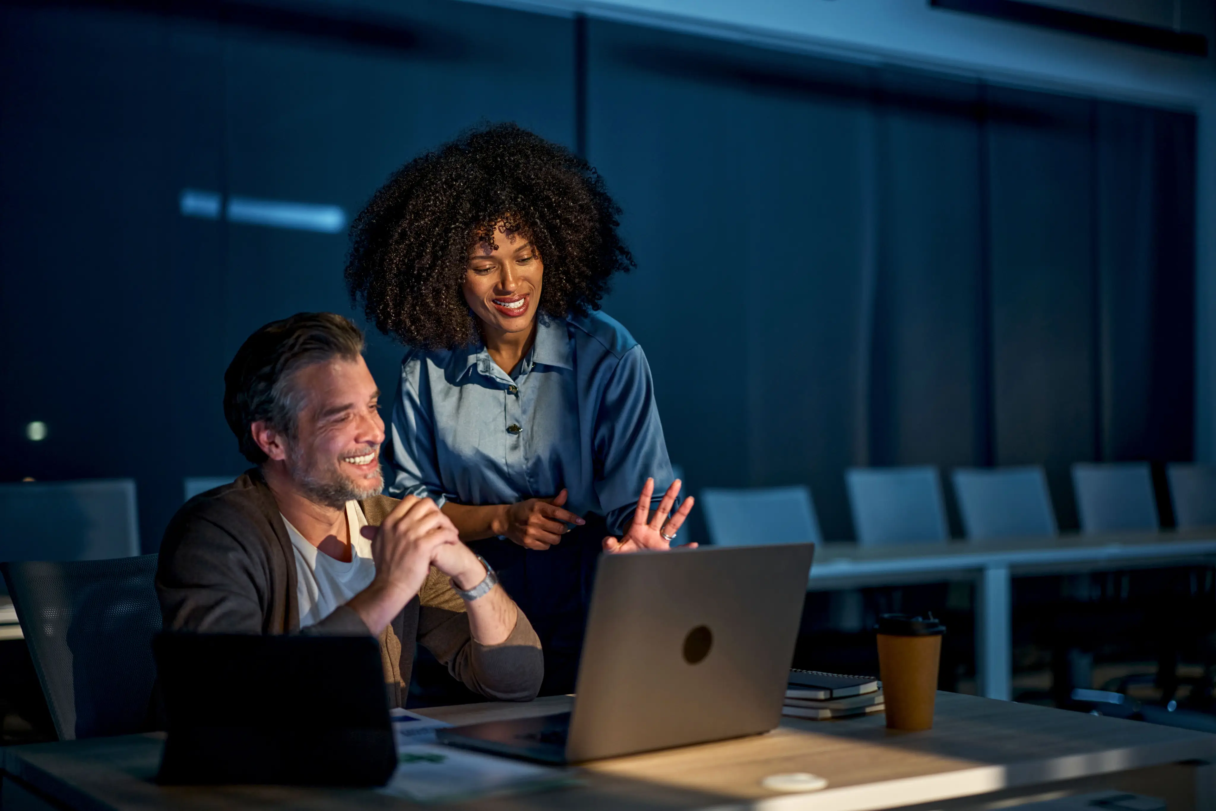 Two colleagues reviewing loan data together on a laptop late at night
